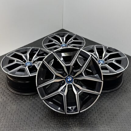 Stacked BMW alloy wheels with black and silver multi-spoke design, centered blue BMW badges, on a textured metal floor.