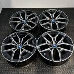 BMW alloy wheels with a black and silver geometric spoke design and blue center badge lying on a textured metal floor surface
