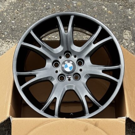 Close-up of a gray BMW alloy wheel resting in a cardboard box on a concrete surface