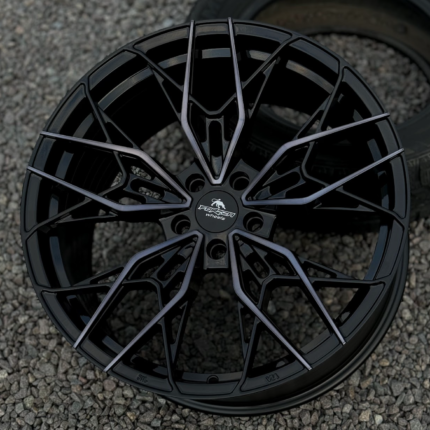 Close-up of a black, multi-spoke alloy wheel with a detailed geometric design and a center cap reading 'FORZA wheels' on a gravel surface.