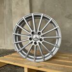 Partial view of a silver alloy car wheel leaning on a wooden pallet outdoors, Mercedes emblem in the center.