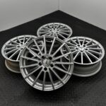 Pile of silver multi-spoke alloy wheels on a black diamond-plate floor, close-up shot.