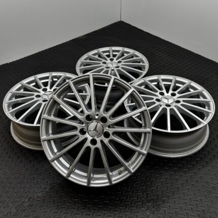Pile of silver multi-spoke alloy wheels on a black diamond-plate floor, close-up shot.