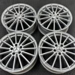 Four silver Mercedes alloy wheels with multi-spoke design arranged on a dark textured surface.