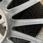 Close-up of a silver automotive component with 'MADE IN POLAND' embossed; a tire tread is visible in the background.