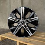 Close-up of a glossy black Mercedes-Benz alloy wheel with silver spokes on wooden pallets.
