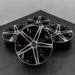 Group of glossy black and silver Mercedes-Benz alloy wheels arranged on a textured metal floor.