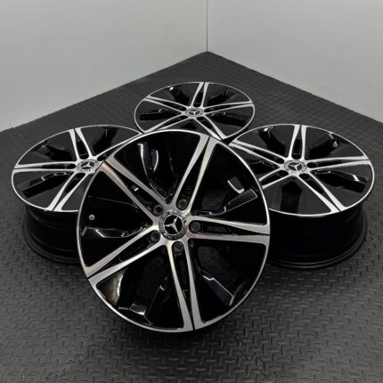 Group of glossy black and silver Mercedes-Benz alloy wheels arranged on a textured metal floor.