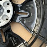 Close-up of a glossy black plastic component with embossed numbers 20 and 21 beside a circular opening and a silver metal ring on the left.
