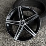 Close-up of a glossy Mercedes-Benz alloy wheel on gray gravel, showing spokes and center cap.