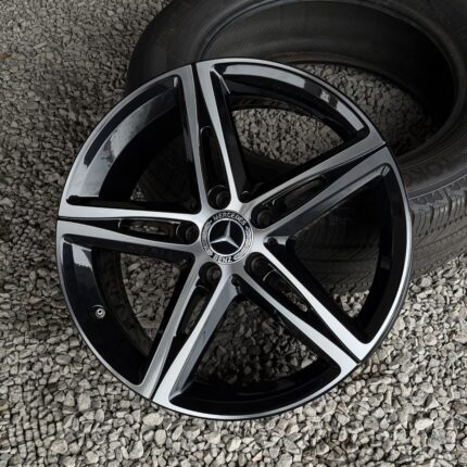 Close-up of a glossy Mercedes-Benz alloy wheel on gray gravel, showing spokes and center cap.