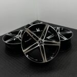 Stacked black and silver Mercedes alloy wheels with chrome accents on a dark textured floor.