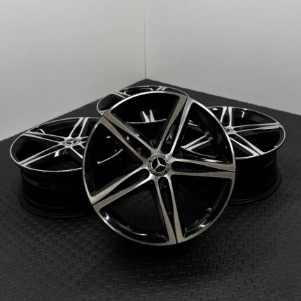 Stacked black and silver Mercedes alloy wheels with chrome accents on a dark textured floor.