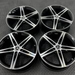 Mercedes-Benz alloy wheels with black and silver spokes laid on a textured metal surface.