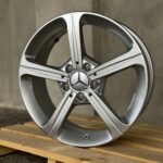 Close-up of a silver alloy wheel with a Mercedes-Benz emblem at the center, resting on wooden pallets.