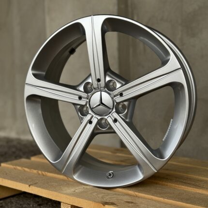 Close-up of a silver alloy wheel with a Mercedes-Benz emblem at the center, resting on wooden pallets.