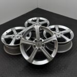 Stack of silver alloy car wheels with Mercedes-Benz logo on a black textured floor.
