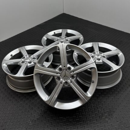 Stack of silver alloy car wheels with Mercedes-Benz logo on a black textured floor.