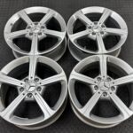 Set of four silver Mercedes alloy wheels with five-spoke design on a dark textured floor.