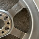 Close-up of a silver alloy wheel showing stamped numbers on the inner hub, with circular bolt holes visible around the edge.
