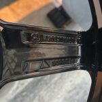 Close-up of a car wheel center cap with a Mercedes-Benz emblem and stamped alphanumeric code in chrome on a dark rim.