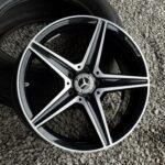 Close-up of a black and silver Mercedes alloy wheel resting on small gray stones/gravel surface, showing the brand emblem at center.