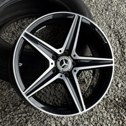 Close-up of a black and silver Mercedes alloy wheel resting on small gray stones/gravel surface, showing the brand emblem at center.