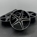 Stack of glossy black and chrome alloy wheels with silver spokes resting on a textured metal floor.