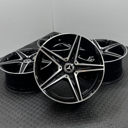 Stack of glossy black and chrome alloy wheels with silver spokes resting on a textured metal floor.