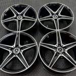 Close-up of glossy black Mercedes-Benz alloy wheels with silver spokes on a textured metal floor