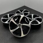 Several Mercedes-Benz alloy rims stacked together on a dark diamond-plate floor, visible hub logos at center caps.