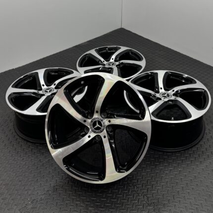 Several Mercedes-Benz alloy rims stacked together on a dark diamond-plate floor, visible hub logos at center caps.