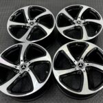 Mercedes-Benz alloy wheels with black and silver spokes laid flat on a textured metal surface, close-up look at rims and center logos.