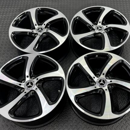 Mercedes-Benz alloy wheels with black and silver spokes laid flat on a textured metal surface, close-up look at rims and center logos.