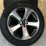 Close-up of a black tire mounted on a silver alloy wheel, showing tread and lug nuts visible.