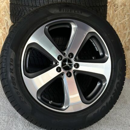 Close-up of a black tire mounted on a silver alloy wheel, showing tread and lug nuts visible.