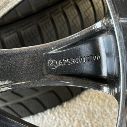Close-up of a black car wheel/rim with a tire, showing engraved numbers and a small emblem on the rim edge.
