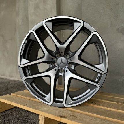 Close-up of a silver and black alloy car wheel with a Mercedes emblem, resting on wooden pallets outdoors.
