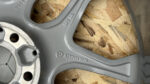 Close-up of a gray alloy wheel rim with circular lug holes and stamped numbers, laying on plywood.