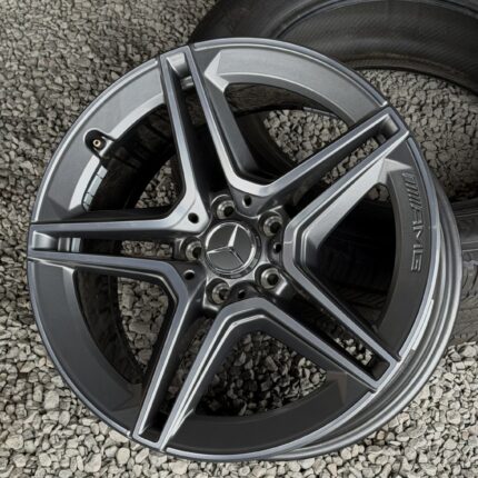 Close-up of a silver alloy wheel resting on gravel stones with part of a tire visible