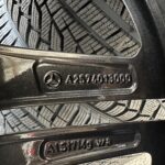 Close-up of stacked tire treads with zigzag patterns beside a dark vehicle surface, showing dirt and grime around the wheel area.