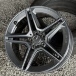 Close-up of a silver alloy car wheel with a tire on a gravel surface. Focus on the rim's metallic finish and design.
