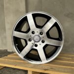 Close-up of a silver Mercedes-Benz alloy wheel with black spokes on a wooden pallet.