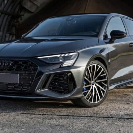 Front three-quarter view of a dark gray Audi SUV with a large black grille and multi-spoke wheels in an outdoor setting.