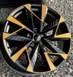 Close-up of a black and orange multi-spoke alloy wheel on gravel.