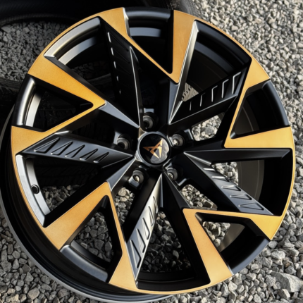 Close-up of a black and orange multi-spoke alloy wheel on gravel.