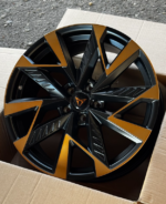 Black and orange multi-spoke alloy wheel in a cardboard box, showing a modern, angular design on a car wheel rim.