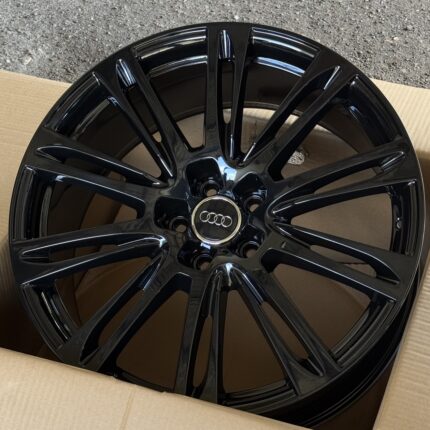 Black glossy Audi alloy wheel with a multi-spoke design and Audi center cap in a cardboard box.