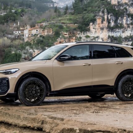 Beige Audi SUV parked on a rocky riverside with a hillside and cliff behind it.