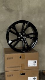 Black glossy alloy Audi wheel with multiple spokes resting on brown cardboard boxes against a concrete wall